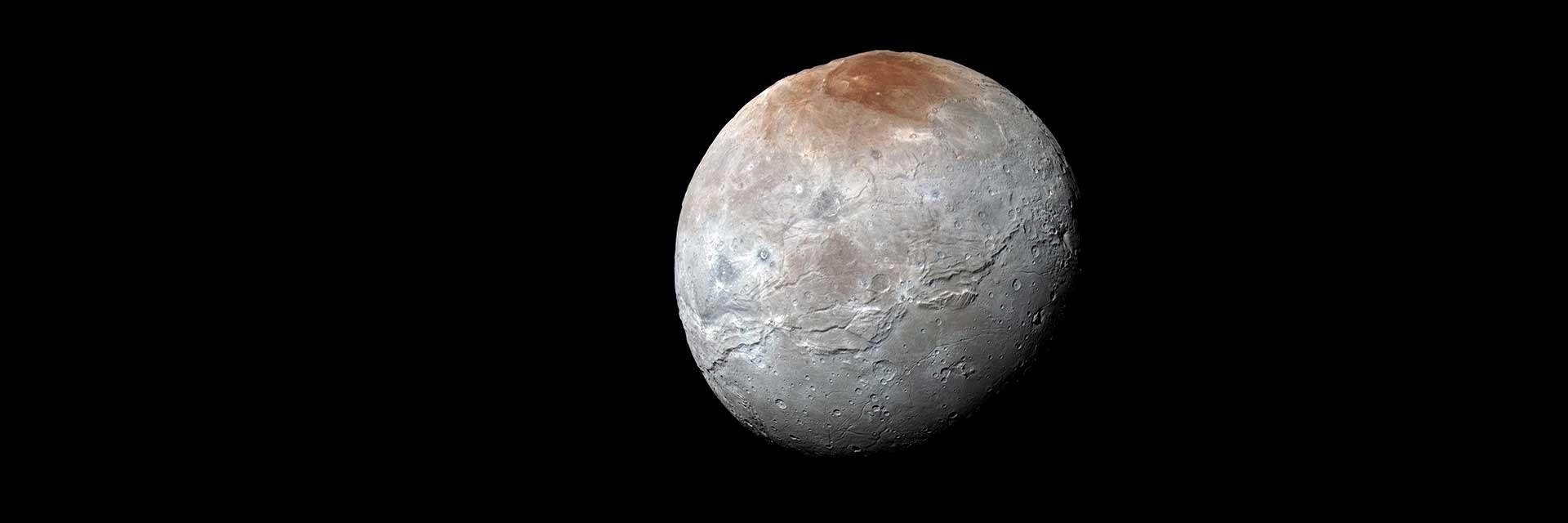 A full globe view of Pluton's moon, Charon. The moon is gray with a reddish cap.