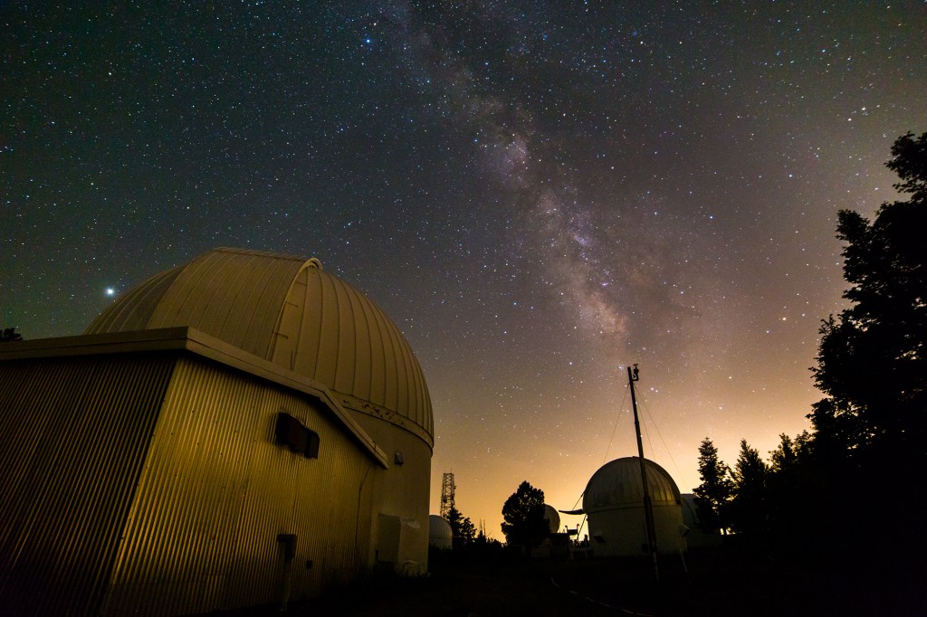 A starry night sky with a telescope in the foreground.
